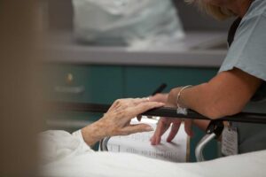 Two older adults sit with a caregiver, reviewing a medication list together at a kitchen table.